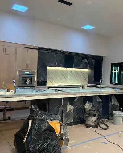 Kitchen at the end of construction, with cabinets wrapped in plastic and tools and bags on the floor
